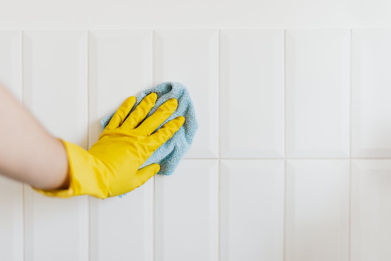 why-choose-us Crop anonymous housekeeper in yellow gloves cleaning white tiled wall using rag in bathroom