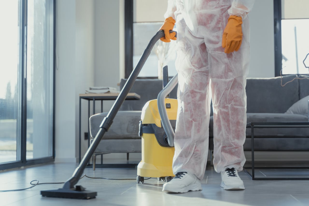 gallery-2 A cleaner in protective coveralls and gloves vacuuming a modern living room.
